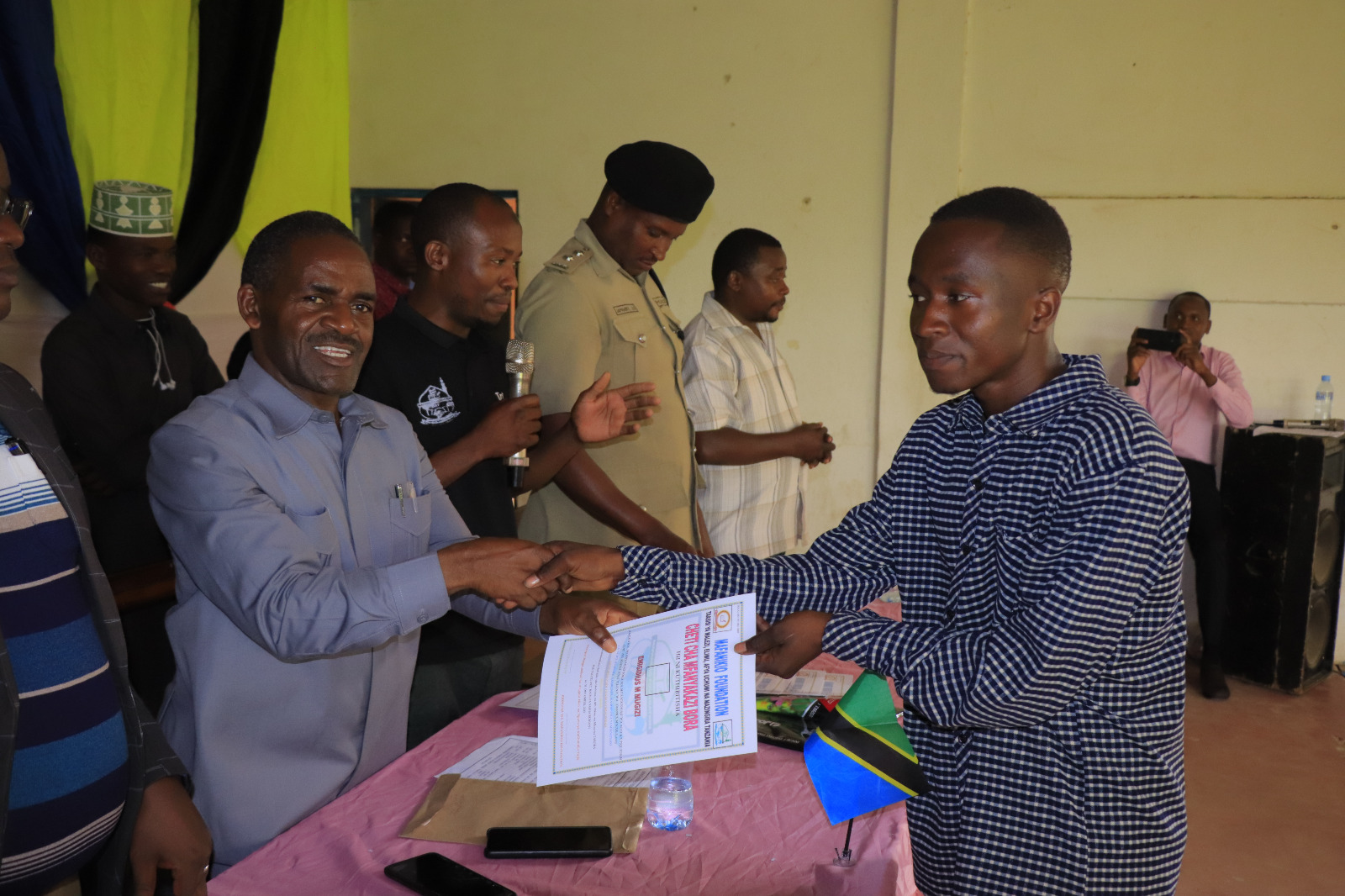 Photos of Mafanikio Foundation volunteers receiving certificates of honor from the Regional Education Officer of Tabora, Mr. Juma Japhet Kaponda, on behalf of the Regional Commissioner of Tabora, for successfully ensuring that all primary school graduates receive special training. Additionally, they launched the campaign "No Child Left Behind - Quality Education for All