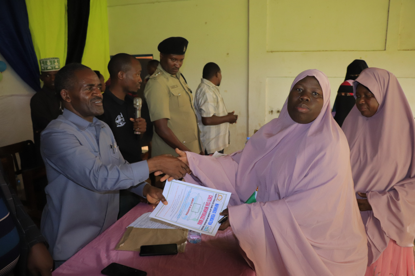 Photos of Mafanikio Foundation volunteers receiving certificates of honor from the Regional Education Officer of Tabora, Mr. Juma Japhet Kaponda, on behalf of the Regional Commissioner of Tabora, for successfully ensuring that all primary school graduates receive special training. Additionally, they launched the campaign "No Child Left Behind - Quality Education for All